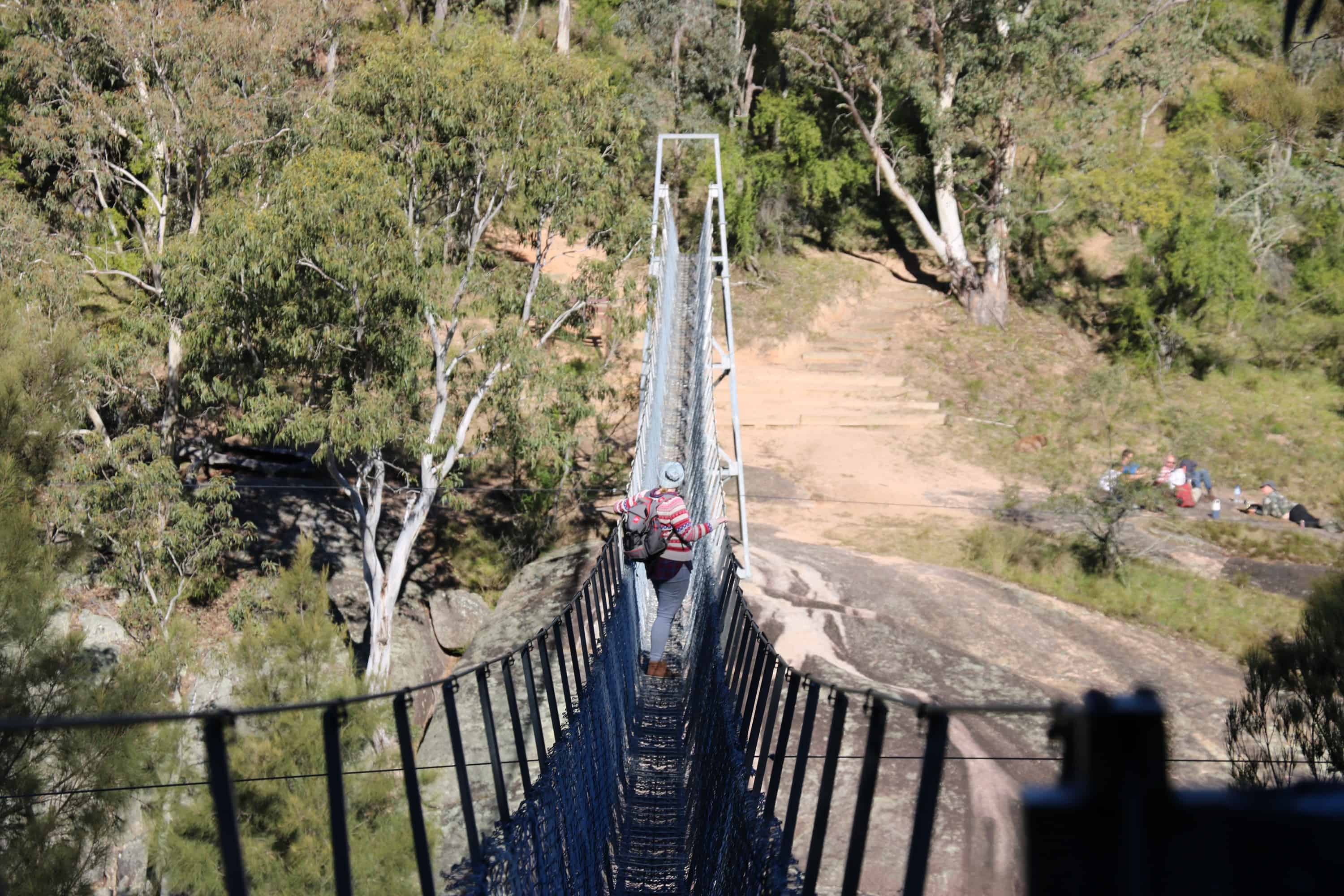 Emma stands on a very narrow metal suspension bridge that extends above the Cox's River