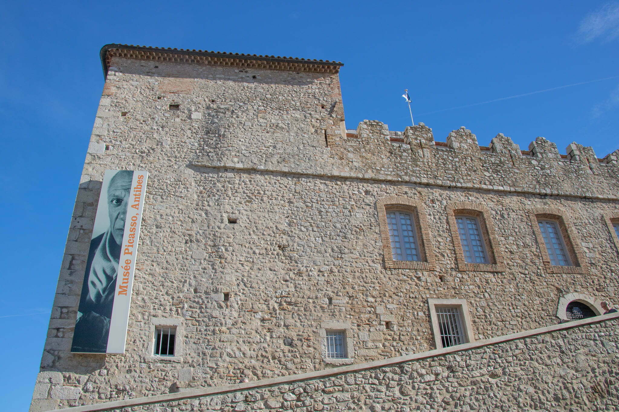 A stone building with a sign hanging on it that reads "Musee Picasso, Antibes"