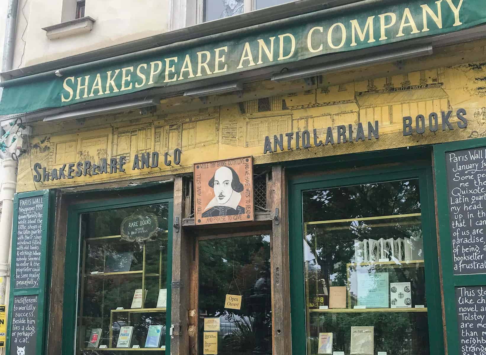 The green and yellow frontage of Shakespeare & Company bookstore with a portrait of Shakespeare hung over the entrance.